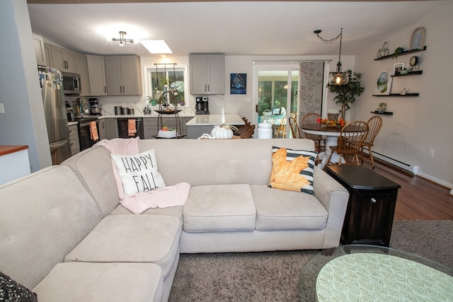 living room with dark wood-type flooring, a skylight, and a baseboard heating unit