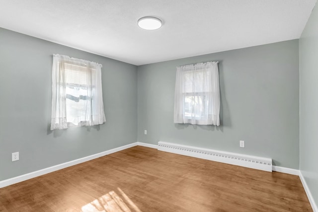 unfurnished room with baseboard heating, a wealth of natural light, and wood-type flooring