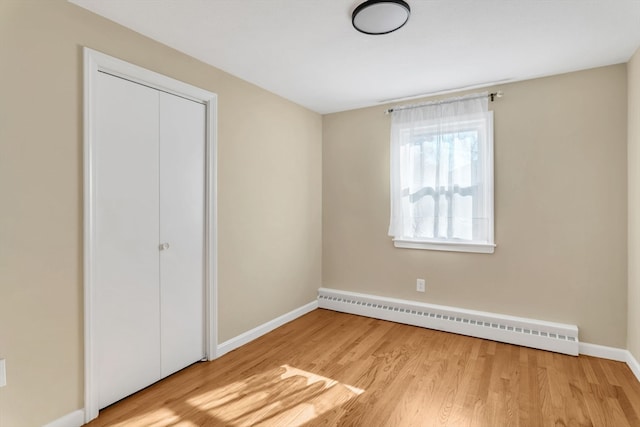 unfurnished bedroom featuring a baseboard heating unit, light hardwood / wood-style floors, and a closet