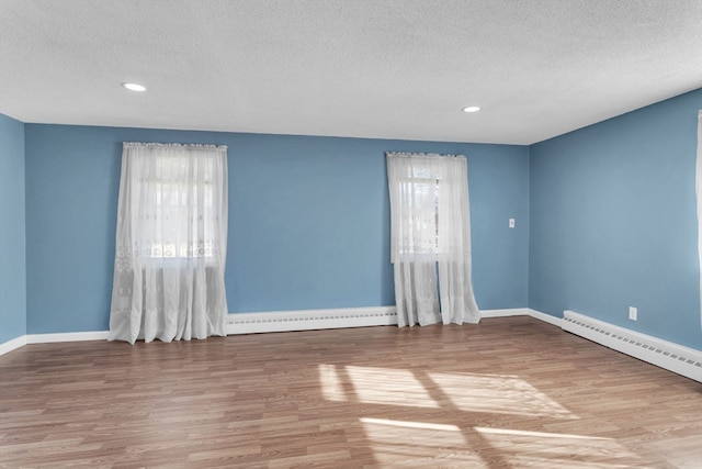 empty room with hardwood / wood-style floors, baseboard heating, and a textured ceiling