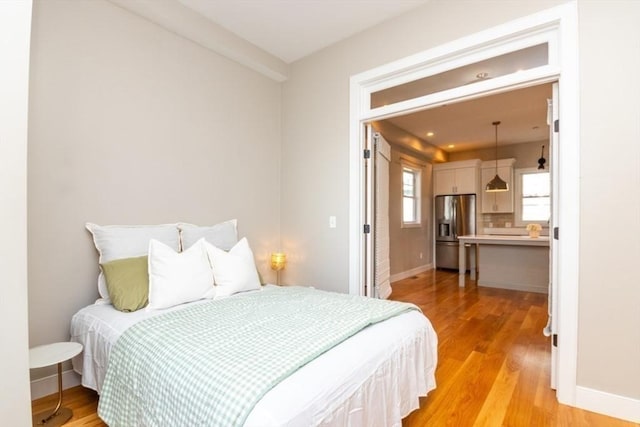 bedroom with light wood-type flooring and stainless steel fridge with ice dispenser