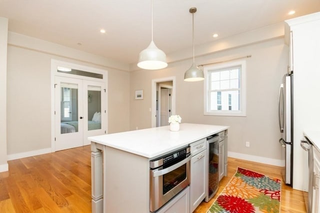 kitchen with stainless steel appliances, white cabinetry, pendant lighting, and beverage cooler