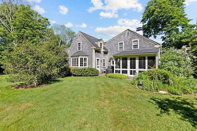 back of house with a chimney, a sunroom, and a lawn