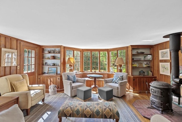 sitting room featuring wood walls, wood finished floors, built in shelves, and a wood stove