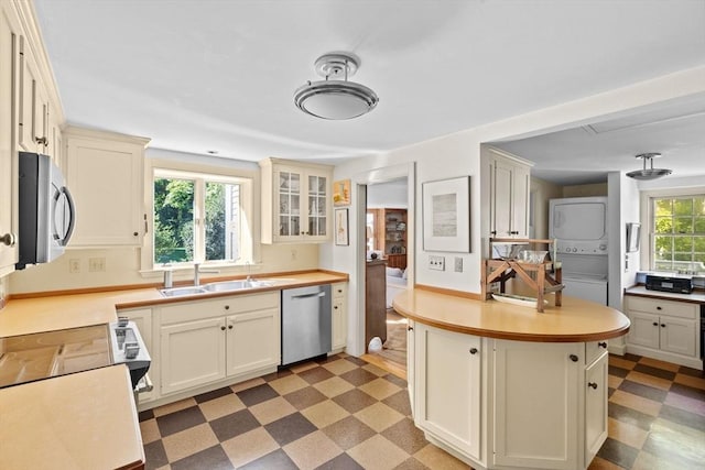kitchen with stainless steel appliances, stacked washer / drying machine, a sink, light flooring, and light countertops