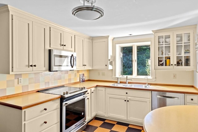 kitchen featuring stainless steel appliances, a sink, light flooring, light countertops, and glass insert cabinets