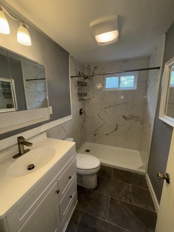 full bathroom featuring toilet, a marble finish shower, and vanity