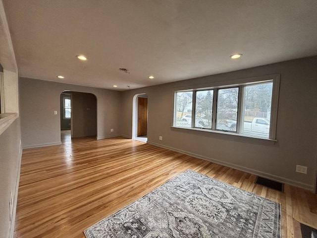 unfurnished living room with light wood-style floors, visible vents, arched walkways, and recessed lighting