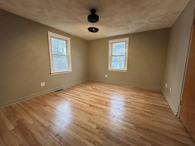 spare room featuring baseboards, a wealth of natural light, light wood-style floors, and visible vents