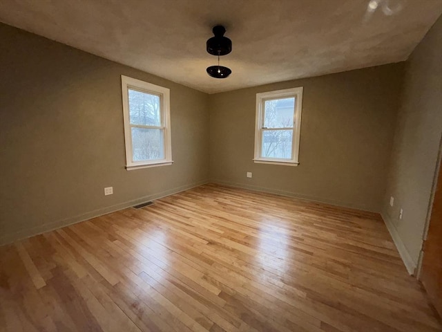 unfurnished room featuring light wood finished floors, a wealth of natural light, visible vents, and baseboards