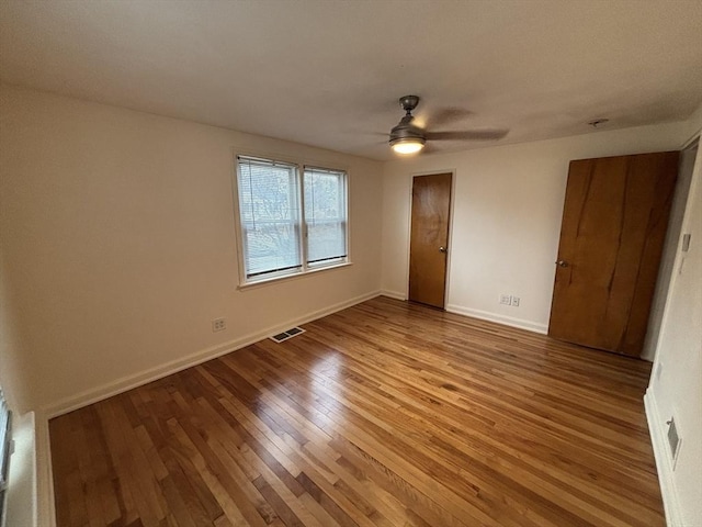 unfurnished bedroom with a ceiling fan, visible vents, wood finished floors, and baseboards