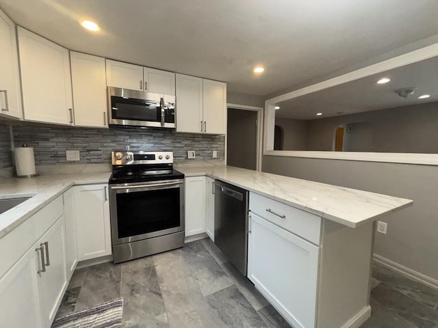 kitchen with a peninsula, decorative backsplash, stainless steel appliances, and white cabinets