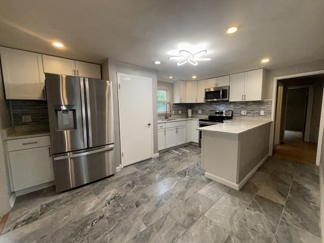 kitchen with a peninsula, backsplash, stainless steel appliances, and a sink