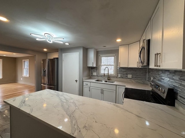 kitchen featuring a sink, stainless steel appliances, white cabinetry, light stone countertops, and tasteful backsplash