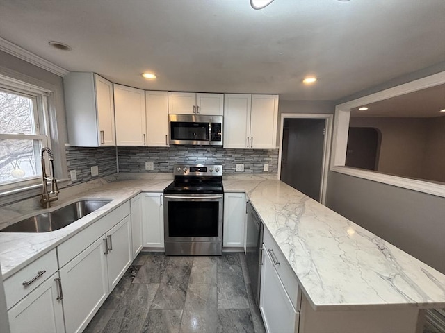 kitchen featuring a sink, white cabinetry, a peninsula, stainless steel appliances, and tasteful backsplash