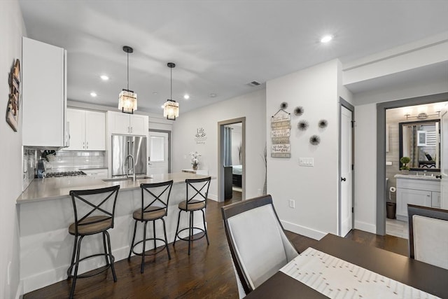 kitchen with a sink, freestanding refrigerator, a peninsula, light countertops, and decorative backsplash