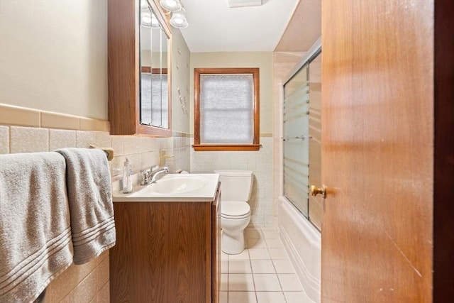 bathroom featuring toilet, shower / bath combination with glass door, tile patterned floors, vanity, and tile walls