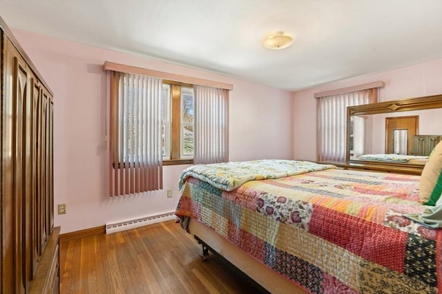 bedroom with a baseboard heating unit, a closet, baseboards, and wood finished floors