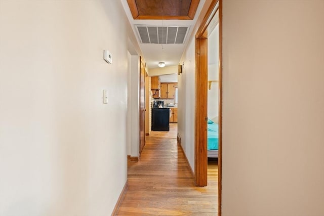 hall with light wood-type flooring, attic access, visible vents, and baseboards