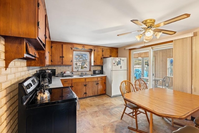 kitchen featuring light countertops, black electric range oven, decorative backsplash, brown cabinetry, and freestanding refrigerator