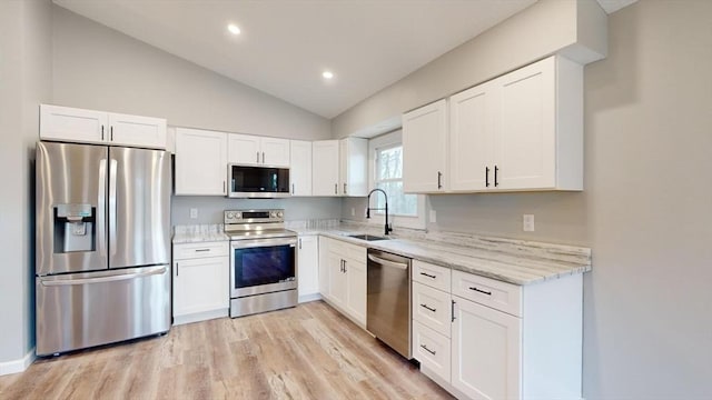 kitchen with lofted ceiling, sink, appliances with stainless steel finishes, light stone countertops, and white cabinets