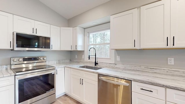 kitchen with white cabinetry, lofted ceiling, sink, light stone counters, and stainless steel appliances