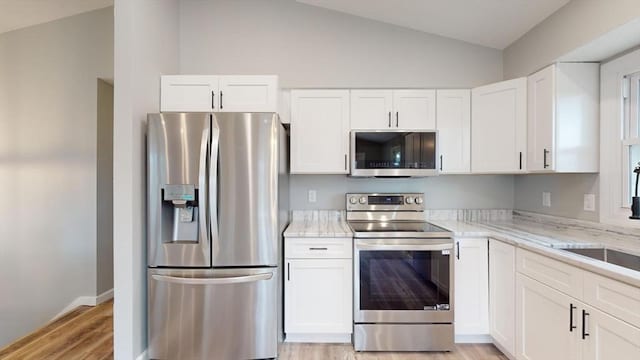 kitchen with white cabinetry, light stone counters, vaulted ceiling, and stainless steel appliances