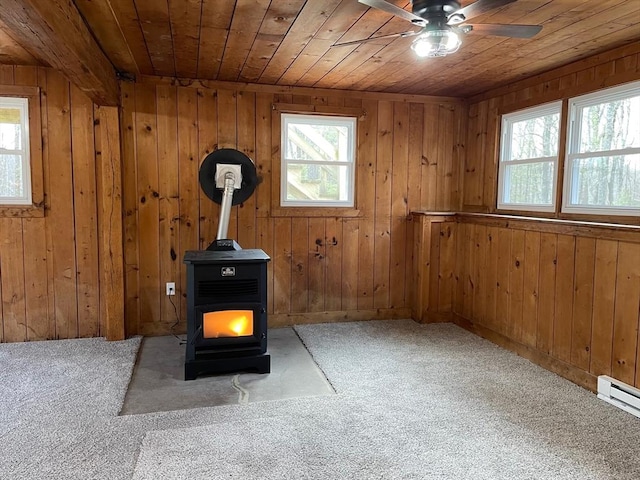 interior space featuring wood walls, wooden ceiling, a wood stove, carpet flooring, and a baseboard heating unit