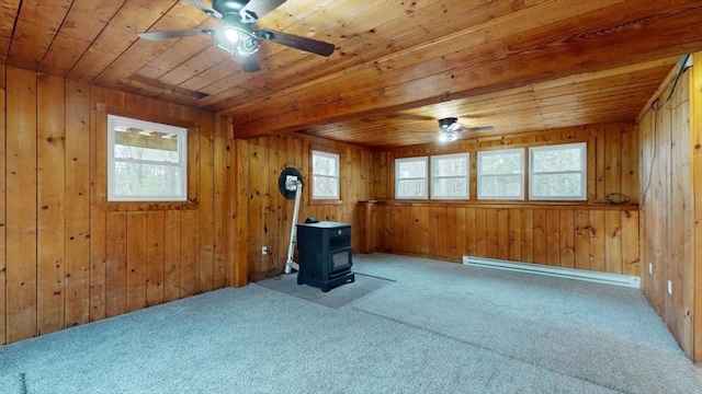 carpeted spare room with wood ceiling, a wood stove, ceiling fan, and baseboard heating