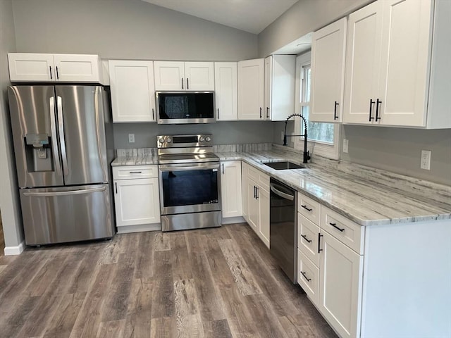 kitchen featuring lofted ceiling, sink, appliances with stainless steel finishes, light stone counters, and white cabinets