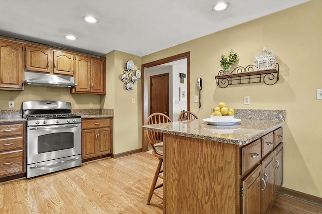 8 Messina Cir, Methuen, MA 01844 - kitchen featuring stainless steel range with gas stovetop, under cabinet range hood, a breakfast bar area, brown cabinets, and recessed lighting