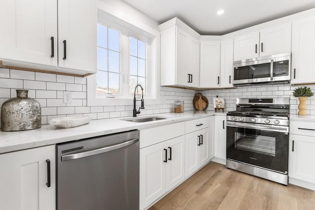 kitchen featuring sink, stainless steel appliances, tasteful backsplash, white cabinets, and light wood-type flooring