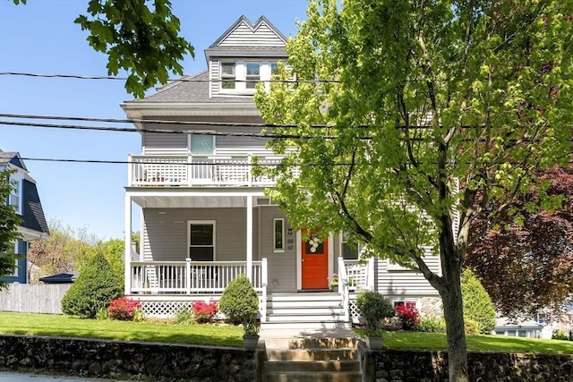 traditional style home featuring a balcony, covered porch, fence, and roof with shingles