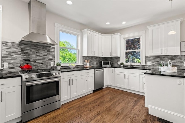 kitchen featuring stainless steel appliances, wall chimney range hood, dark countertops, dark wood-style floors, and recessed lighting