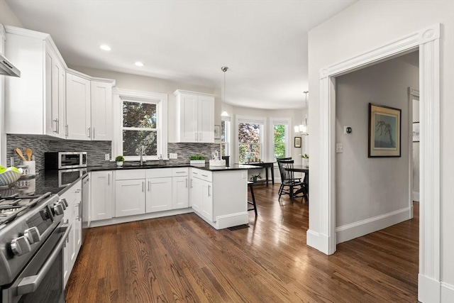 kitchen with tasteful backsplash, appliances with stainless steel finishes, dark wood-style flooring, dark countertops, and white cabinetry