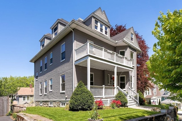 american foursquare style home featuring a balcony, covered porch, and a front yard