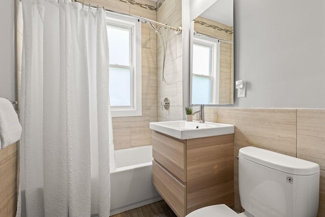 full bathroom with toilet, tile walls, healthy amount of natural light, shower / bath combo, and vanity