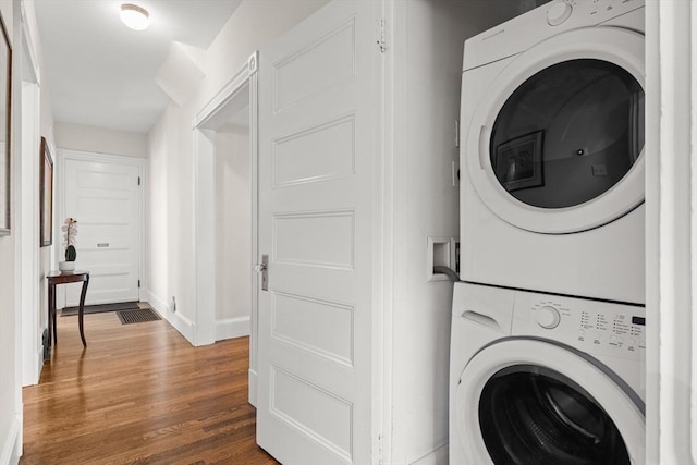 laundry area with estacked washer and dryer, wood finished floors, and baseboards