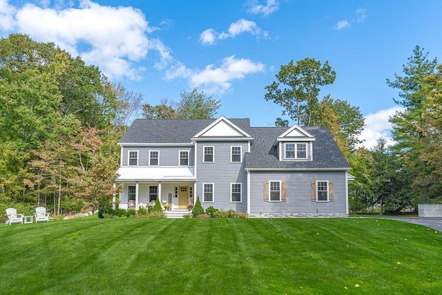 colonial inspired home featuring roof with shingles and a front yard