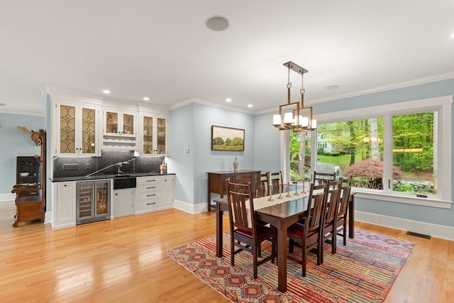 dining area with wine cooler, bar, baseboards, crown molding, and light wood-style flooring