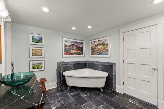 bathroom featuring baseboards, a sink, recessed lighting, and a freestanding tub