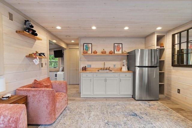 kitchen featuring open shelves, freestanding refrigerator, a sink, light wood-type flooring, and wooden walls
