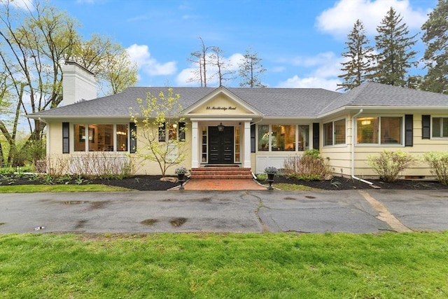 ranch-style home with a chimney, a front yard, and roof with shingles