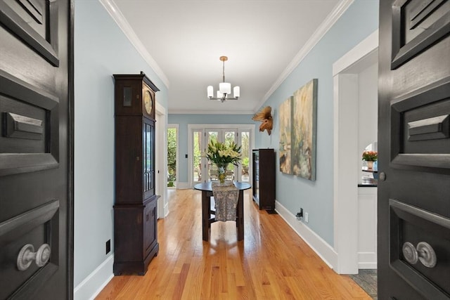 entryway with crown molding, baseboards, light wood-style floors, and a chandelier