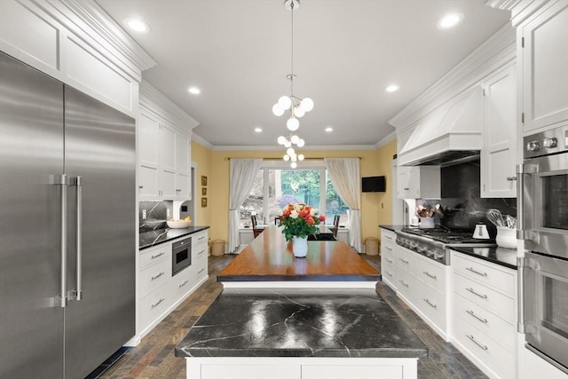 kitchen featuring built in appliances, ornamental molding, a center island, tasteful backsplash, and white cabinets