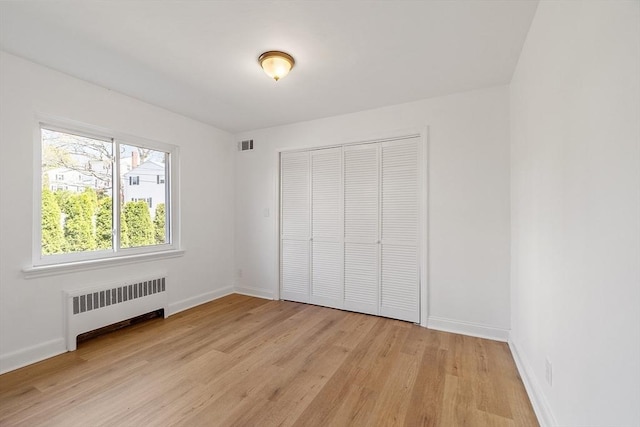 unfurnished bedroom featuring light wood-style flooring, radiator, baseboards, visible vents, and a closet