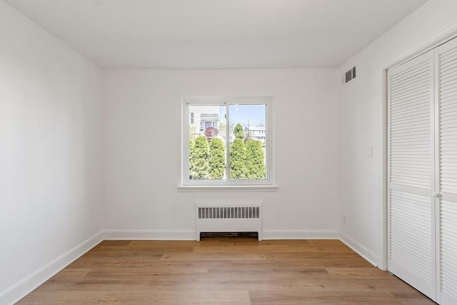 unfurnished bedroom with visible vents, baseboards, a closet, light wood finished floors, and radiator