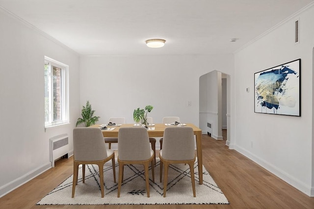 dining space with crown molding, radiator, arched walkways, and light wood-style flooring
