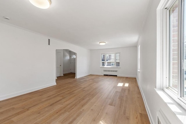 spare room featuring arched walkways, baseboards, radiator, ornamental molding, and light wood-style flooring