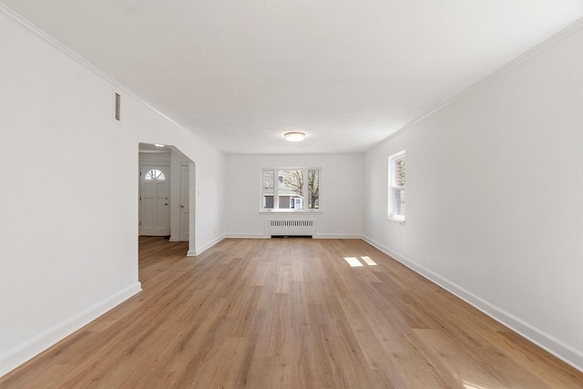 unfurnished living room with visible vents, arched walkways, baseboards, light wood-style floors, and radiator